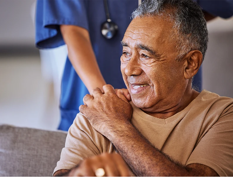 nurse touching shoulder of older man in a beige shirt. he looks comforted.